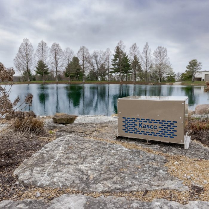 Robust-Aire System compressor cabinet installed beside pond shoreline with lake and trees in background